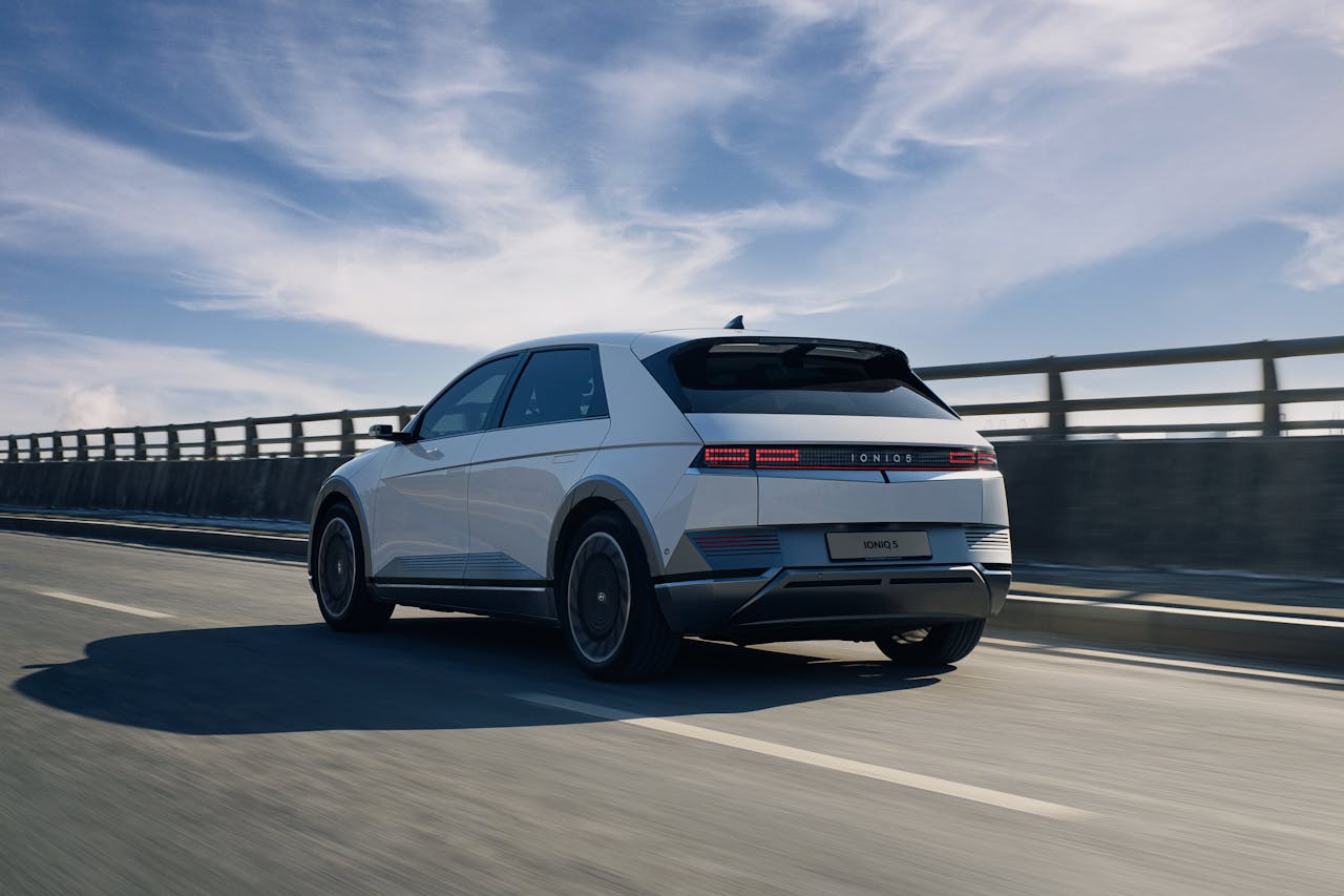 Sleek white electric car driving on an open highway under a bright blue sky.
